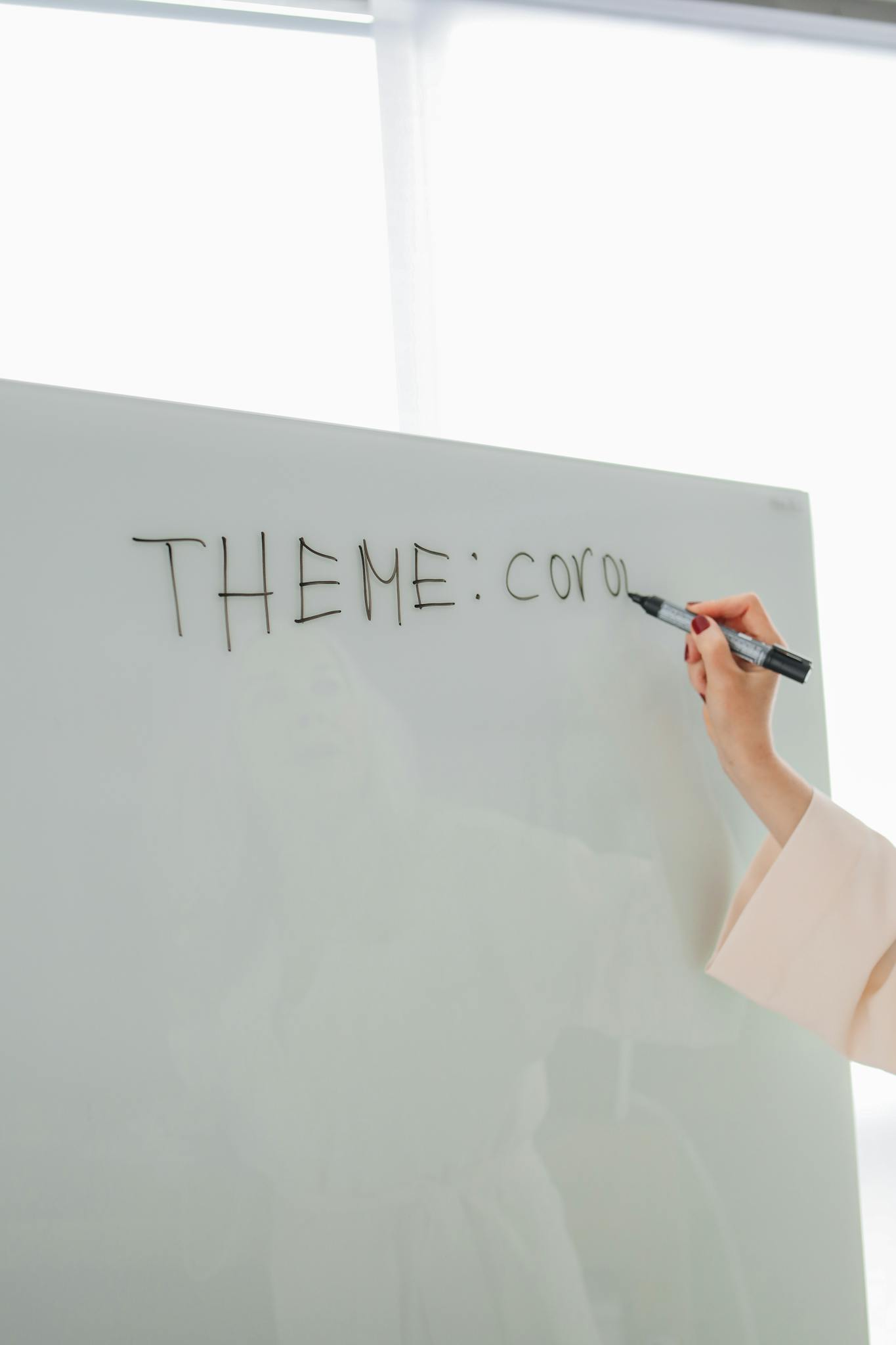 Hand writing 'THEME: cor...' on whiteboard in modern classroom.